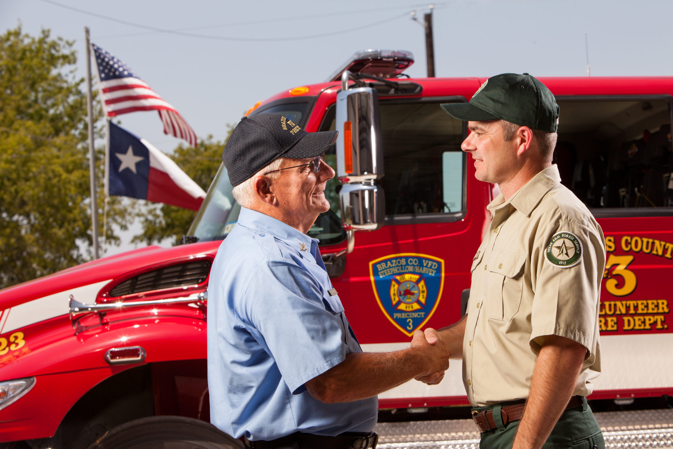 Two men are shaking hands in front of a firetruck